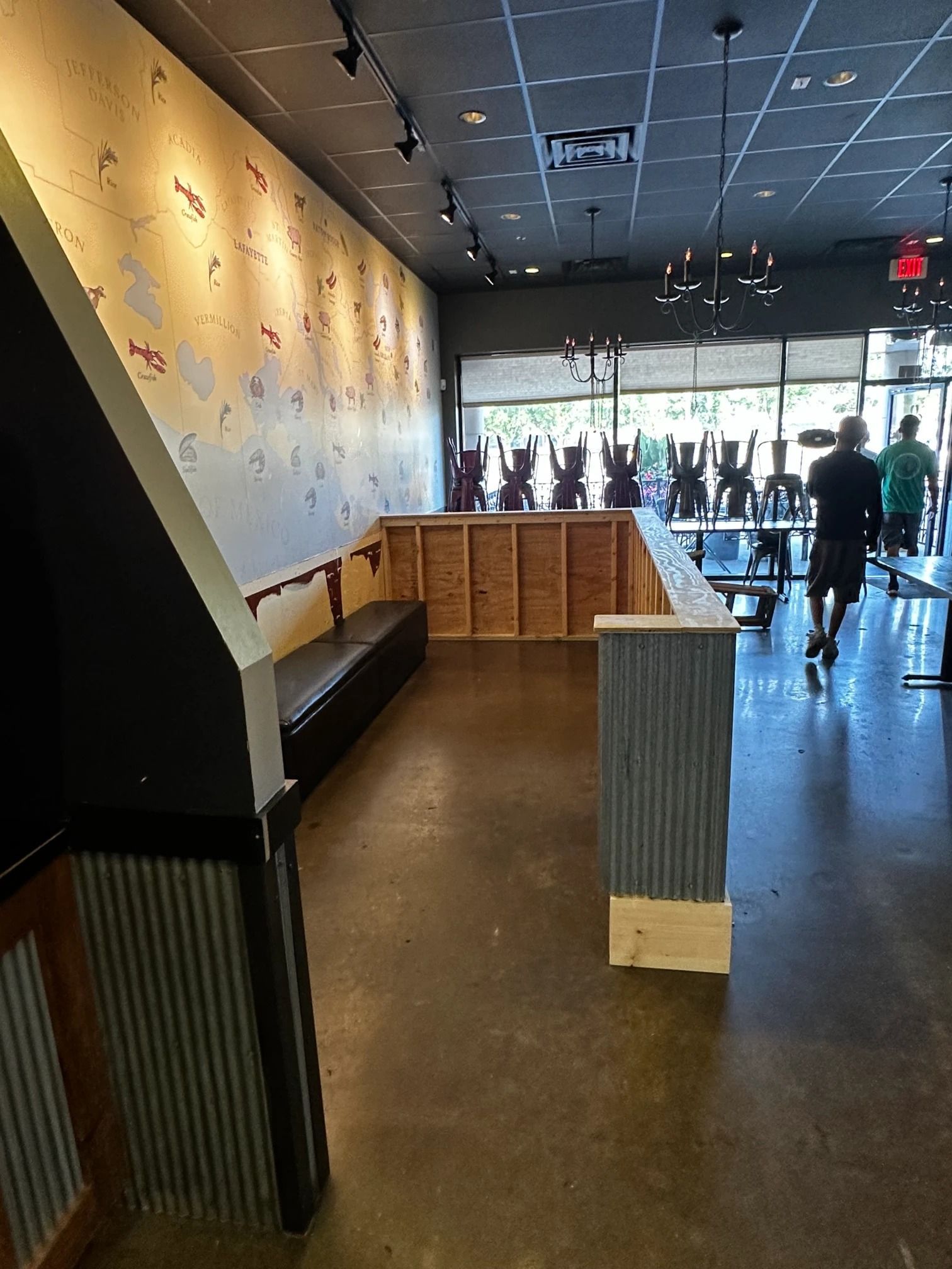 Interior shot of a restaurant with a built-in bench, corrugated metal accents, and people walking by a window.