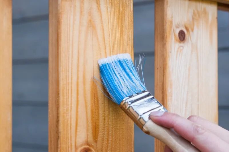 Hand painting wood railing with a blue-bristled brush, showing the wood's grain and natural color.