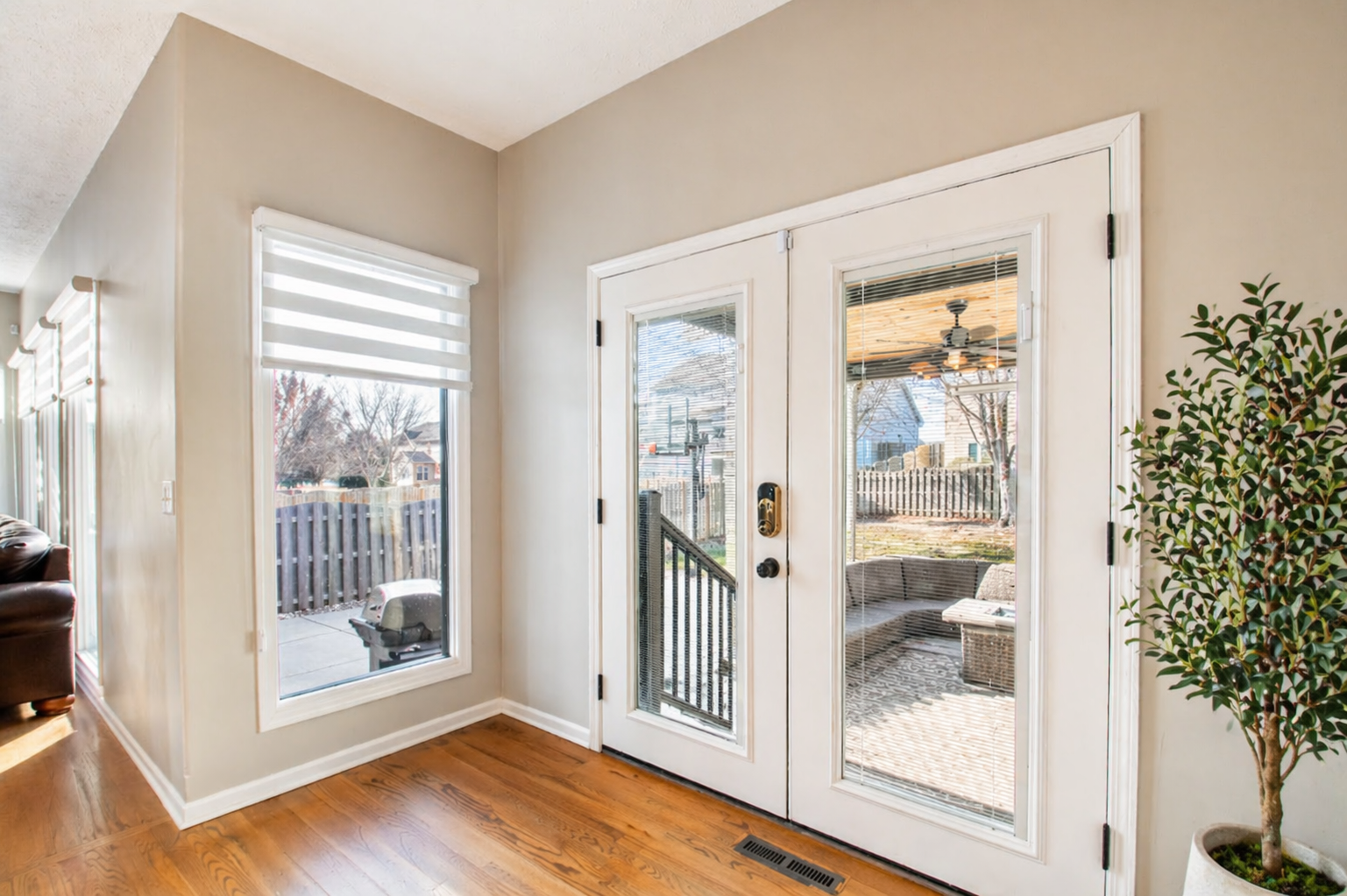 Bright entryway with white French doors, large window, hardwood floor, and potted tree.