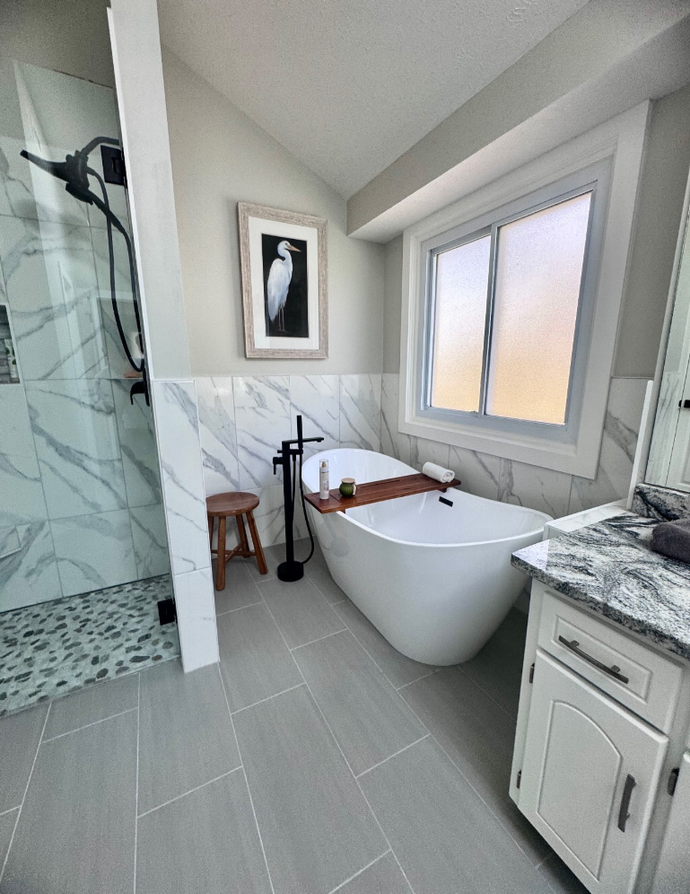 A modern bathroom featuring a white freestanding tub, a walk-in shower with marble tile, and a framed bird art print.