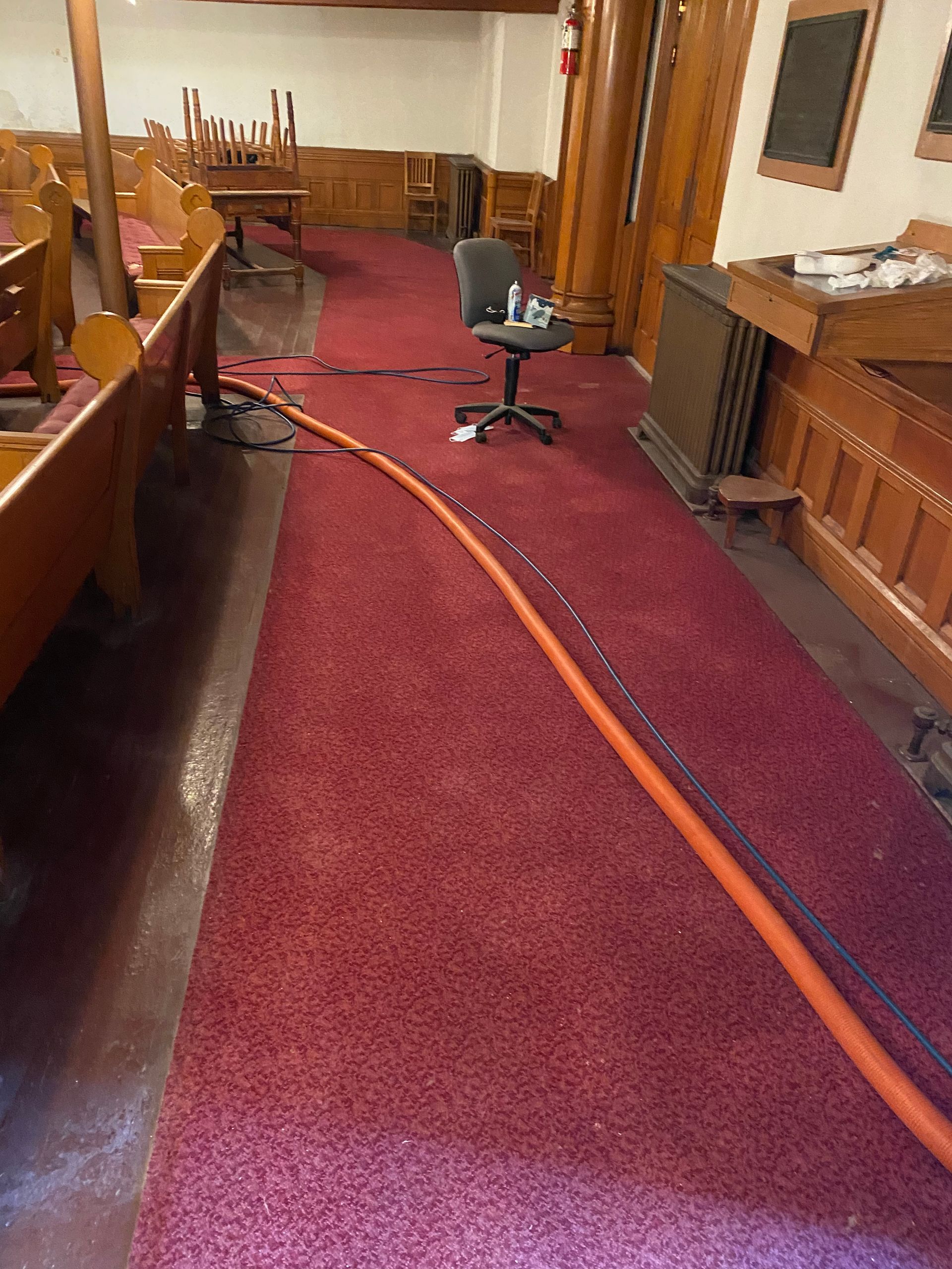 A red carpeted hallway in a church with a chair and a hose.