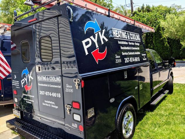 Black PYK Heating & Cooling truck with logo, ladder on top, parked on grass.