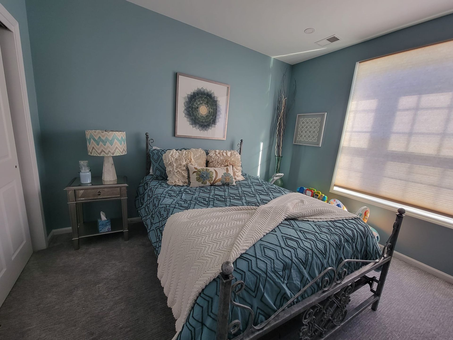 A bedroom with a bed , nightstand , lamp and window.