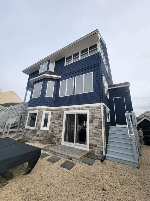 A large blue house with a lot of windows is sitting on top of a gravel lot.