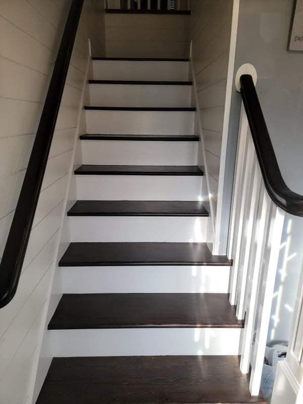 A set of white stairs with dark wooden steps and a black railing