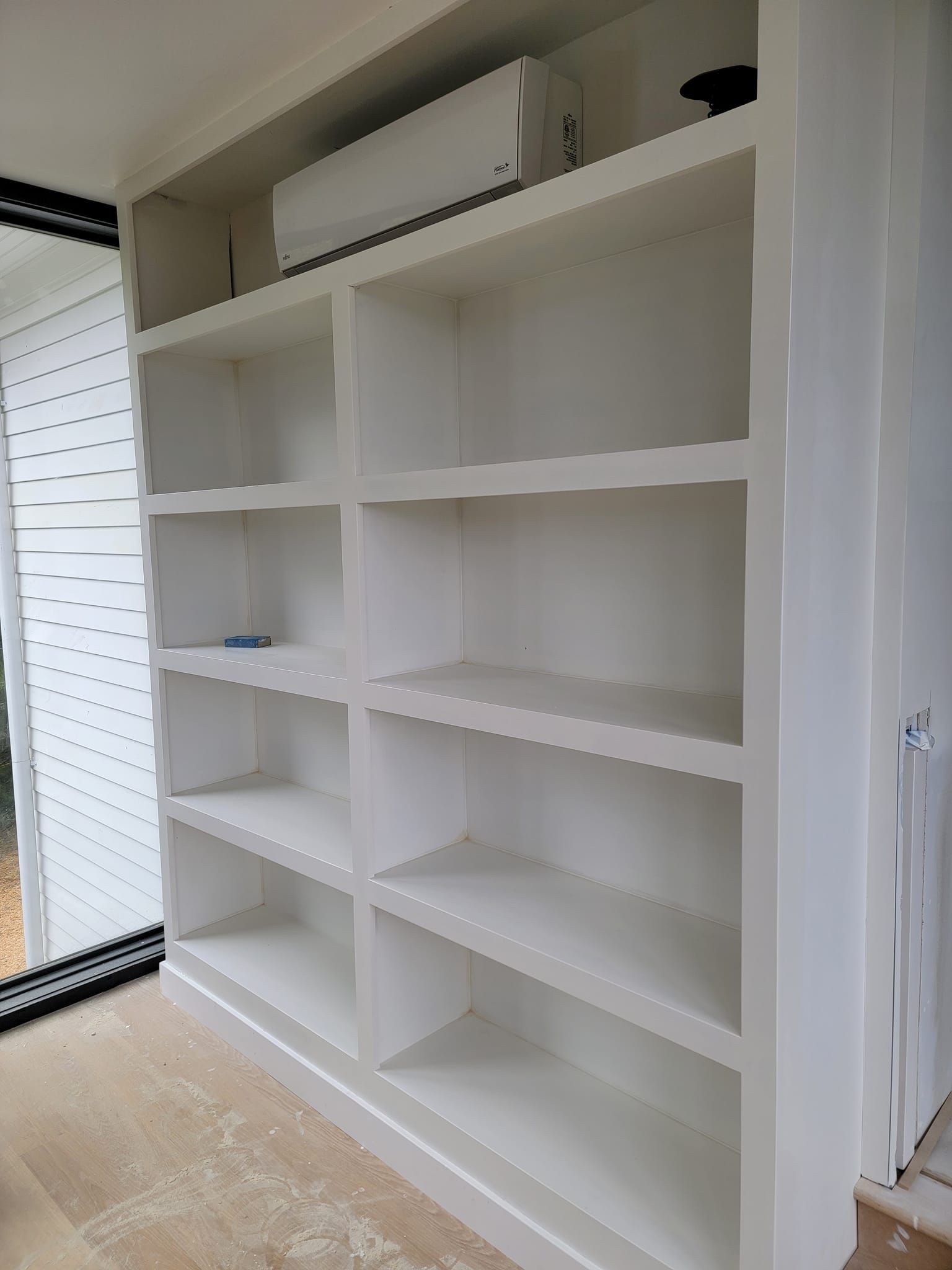A white bookshelf with a air conditioner on top of it in a room.