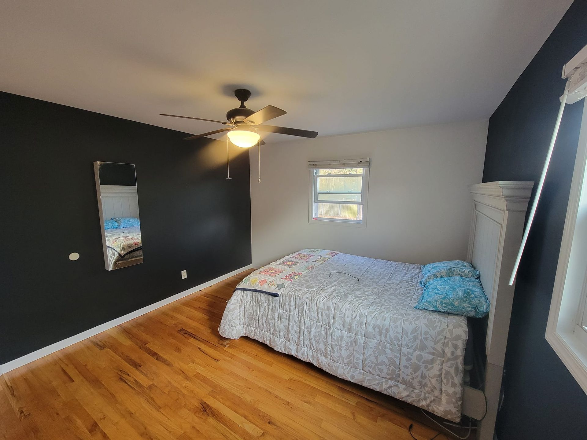 A bedroom with a bed , ceiling fan , mirror and window.