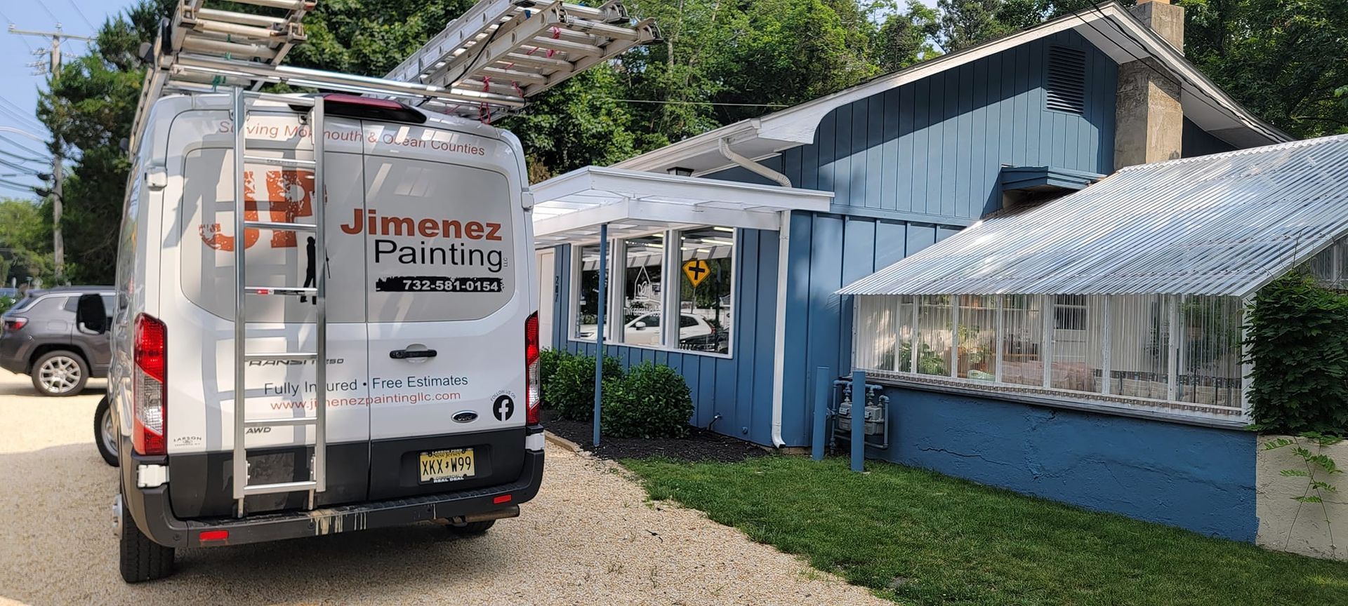 A white van with a ladder on the back is parked in front of a blue house.