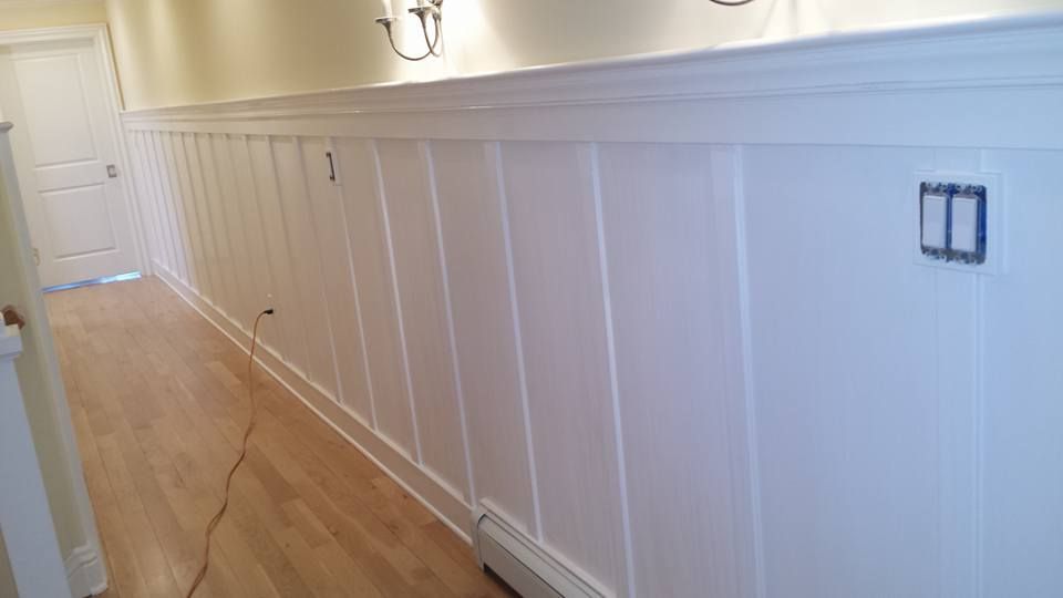 A long hallway with white paneling and hardwood floors.