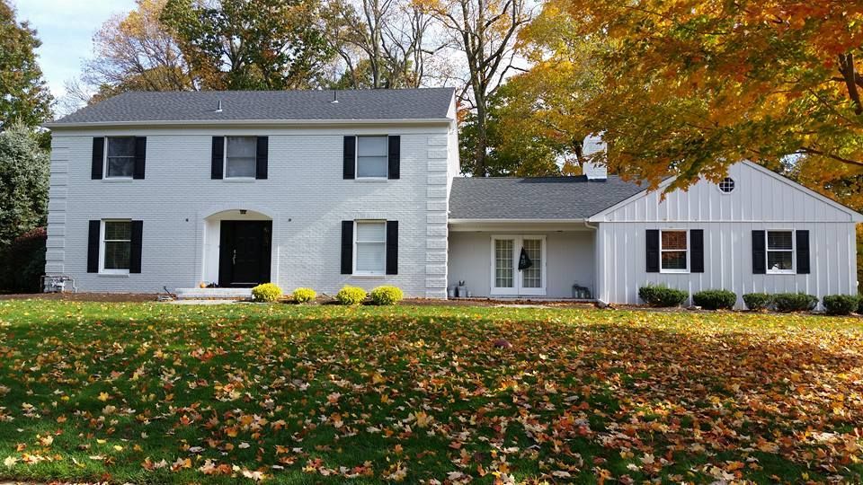 A large white house with black shutters is sitting on top of a lush green lawn.
