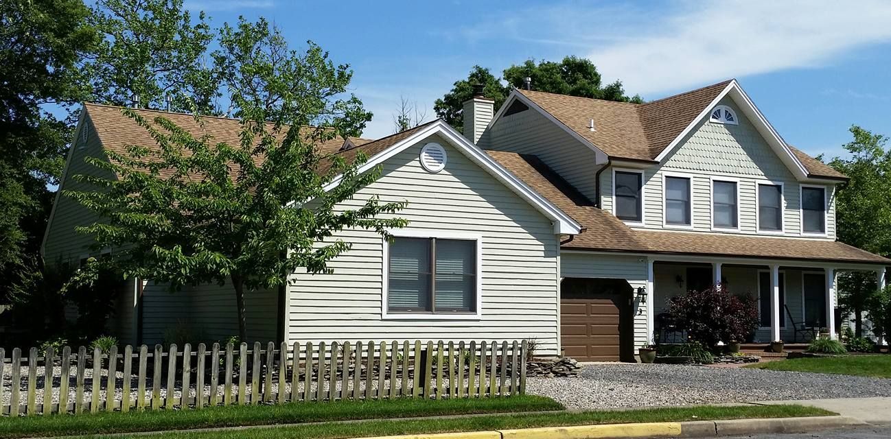 A large white house with a brown roof and a white picket fence