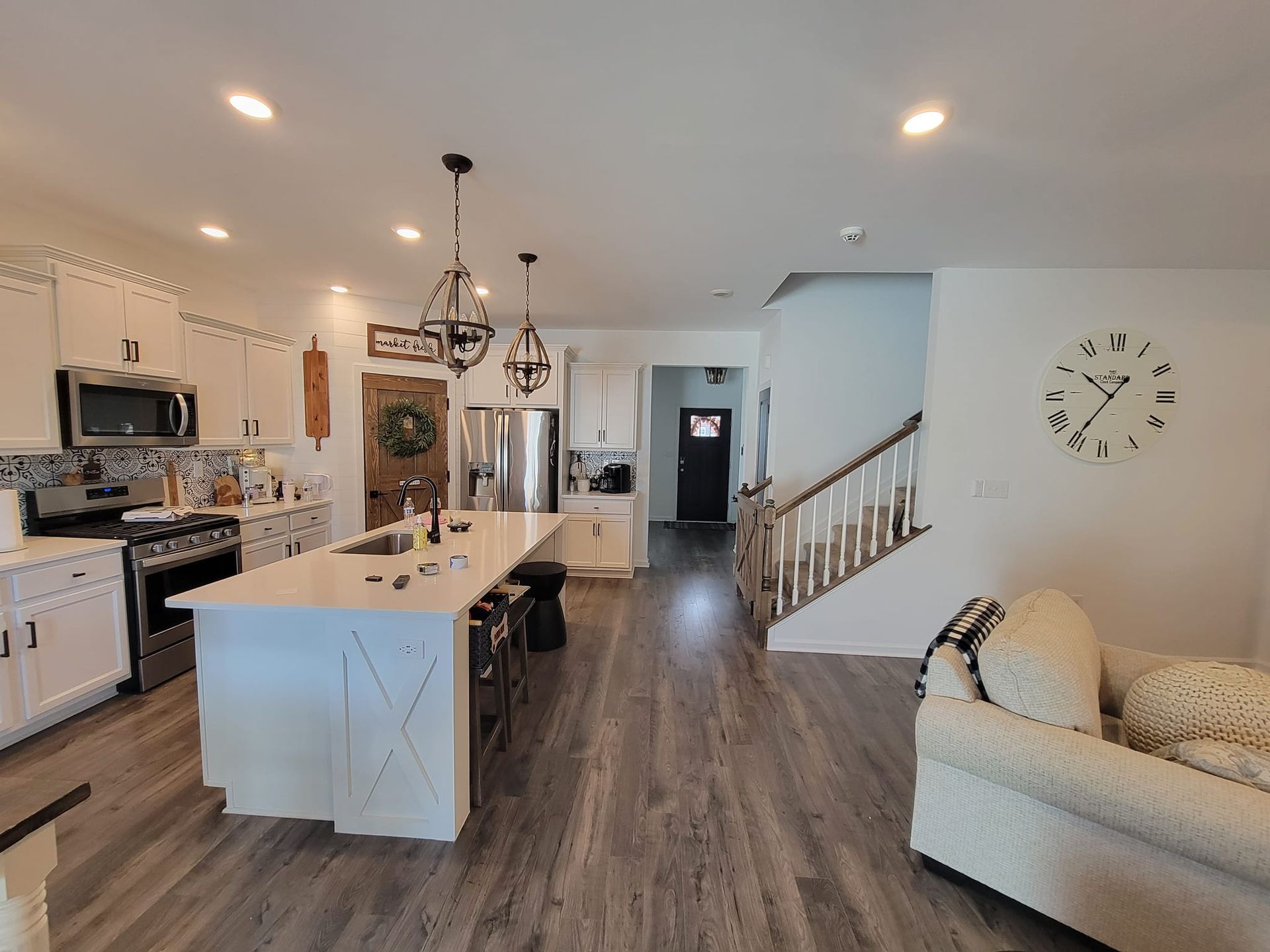A kitchen and living room in a house with a clock on the wall.