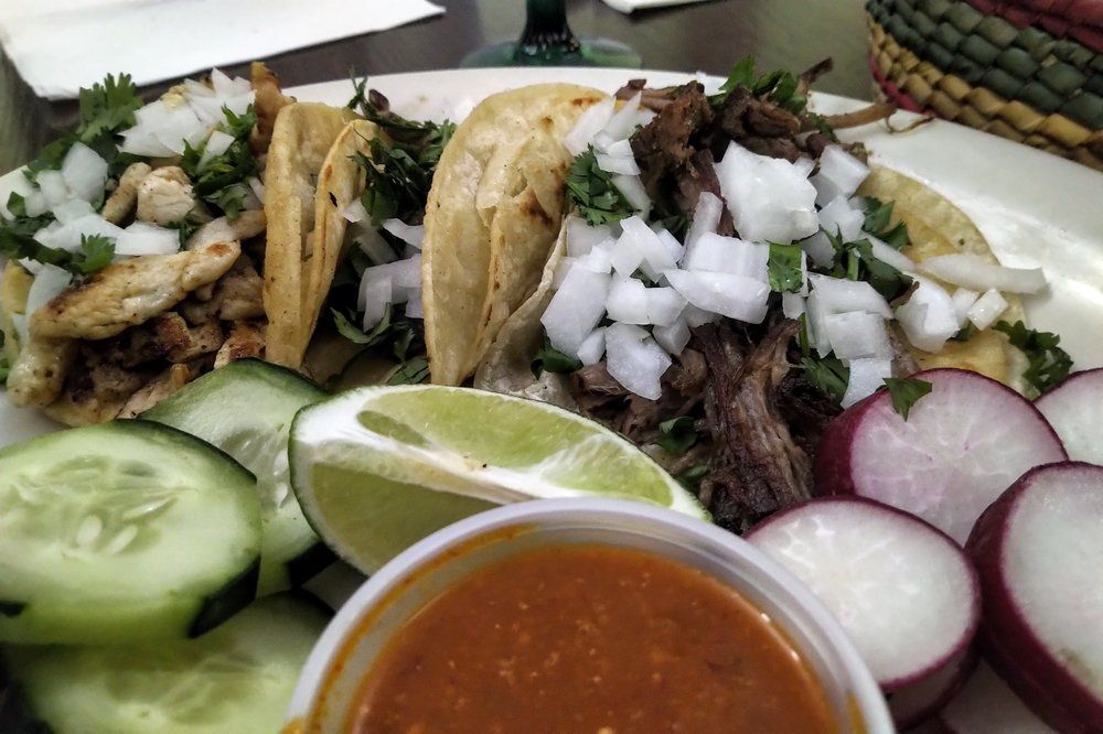 A white plate topped with tacos and vegetables next to a cup of sauce
