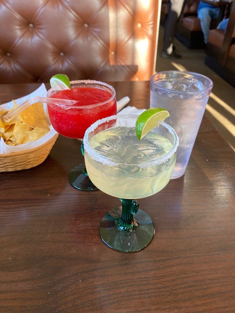 Two margaritas are sitting on a wooden table next to a basket of tortilla chips.