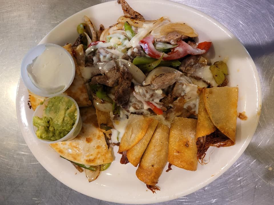 A plate of food with guacamole and sour cream on a table.