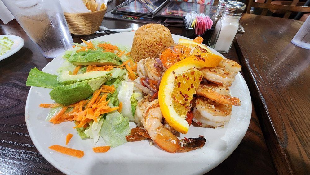 A plate of food with shrimp, rice, and a salad on a table.