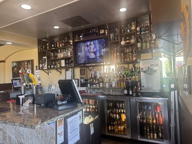 A bar in a restaurant with bottles of alcohol and a television.