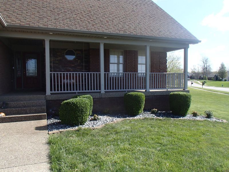Front porch of a brick house with green bushes and a gray railing.