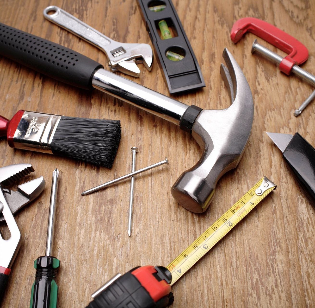 A hammer is surrounded by other tools on a wooden table