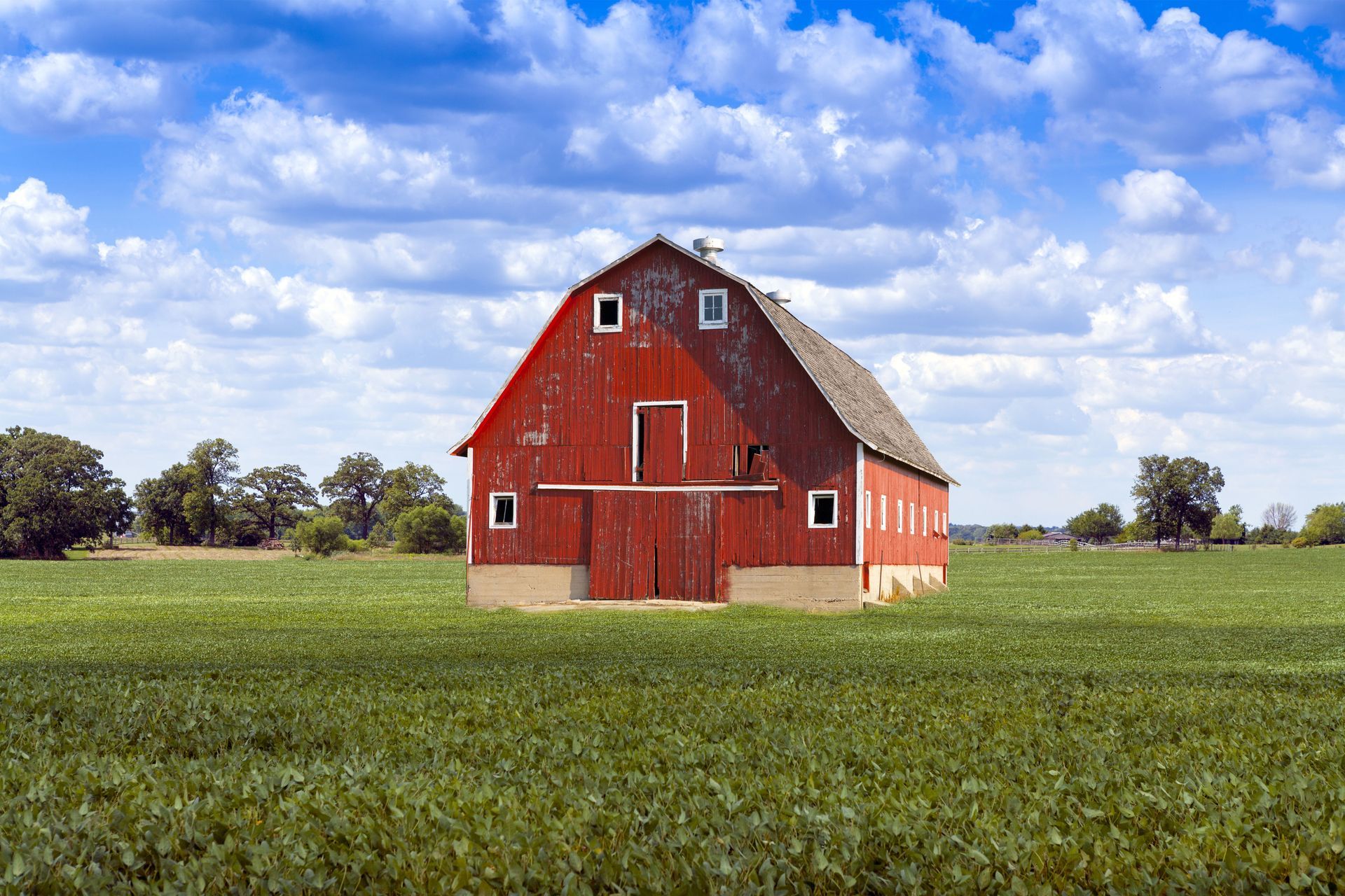 Red barn in a green field under a bright blue sky with scattered clouds
