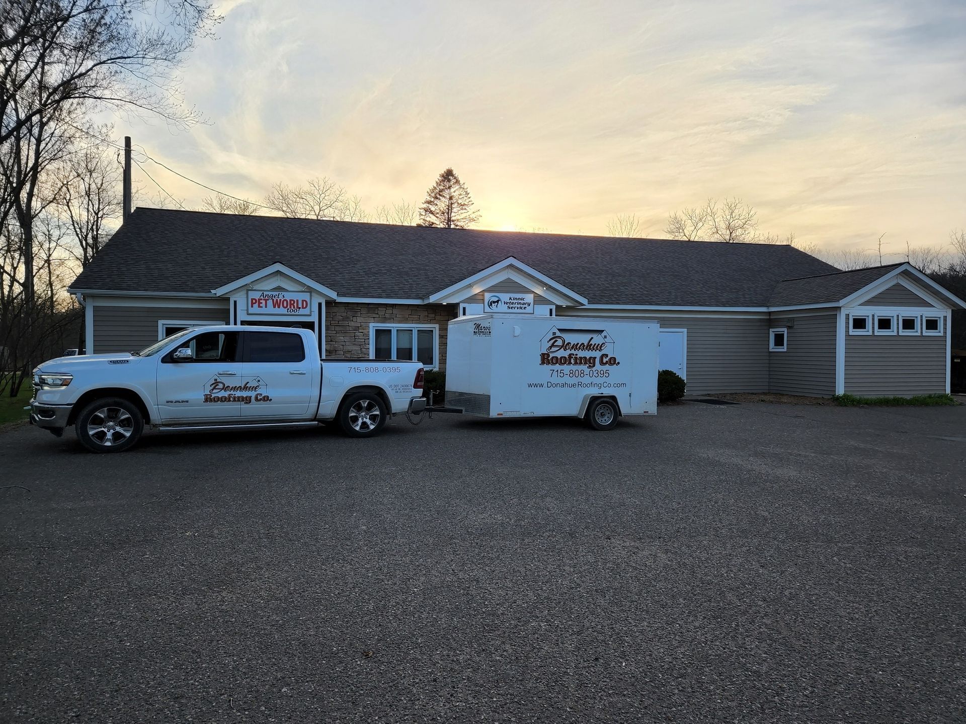 White two-story house with black shutters and a dark roof, set in a green, tree-lined yard.