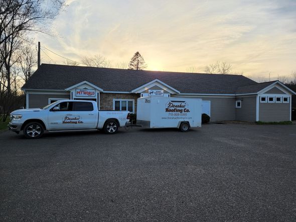 White two-story house with black shutters and a dark roof, set in a green, tree-lined yard.