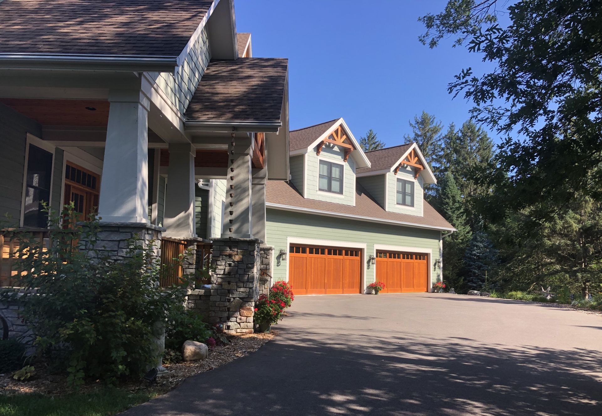 Two-story house with a stone porch, attached garage with wooden doors, and asphalt driveway.