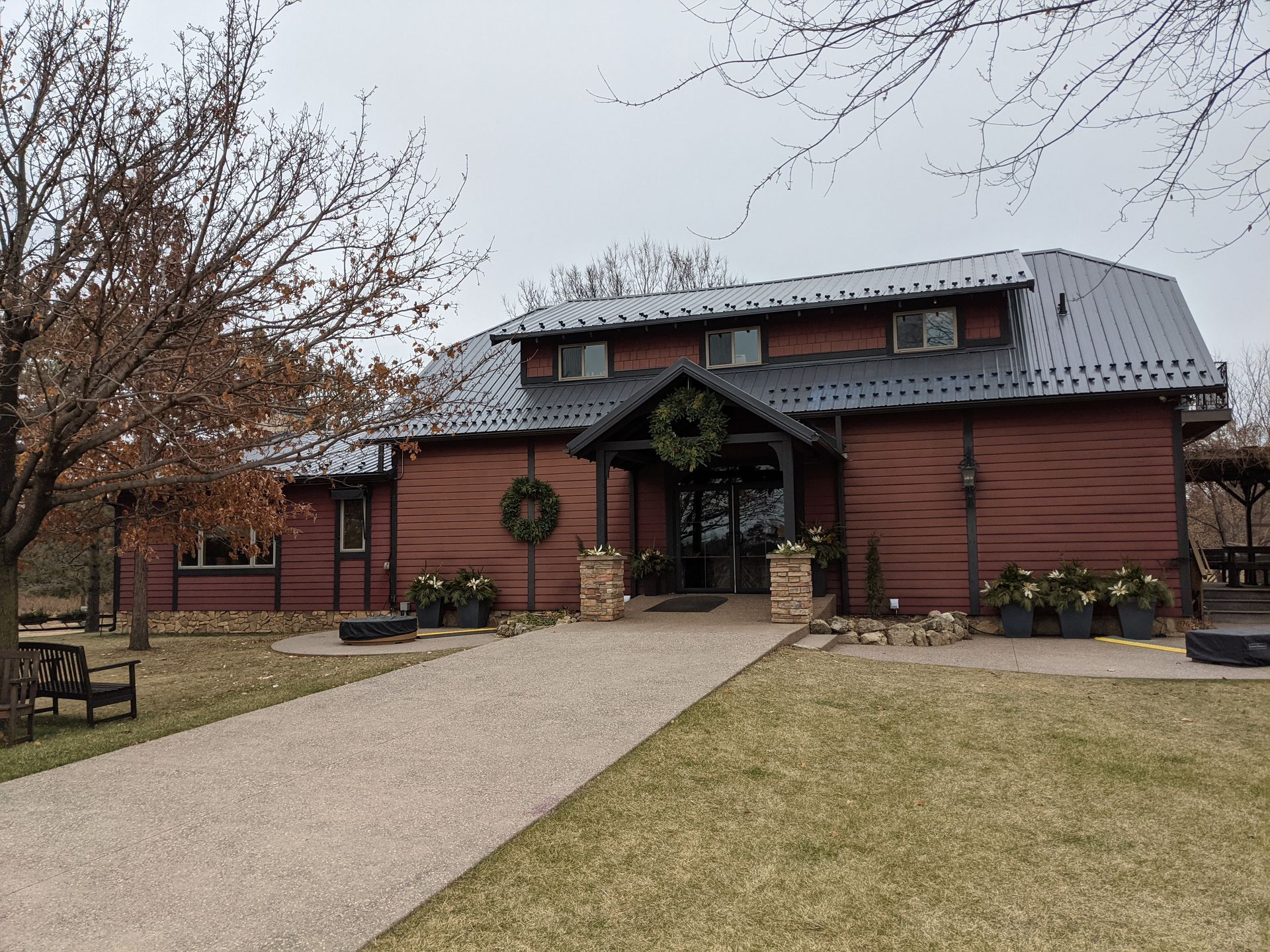 Red wooden building with a gray roof, a stone path leading to the entrance, and a wreath on the door.
