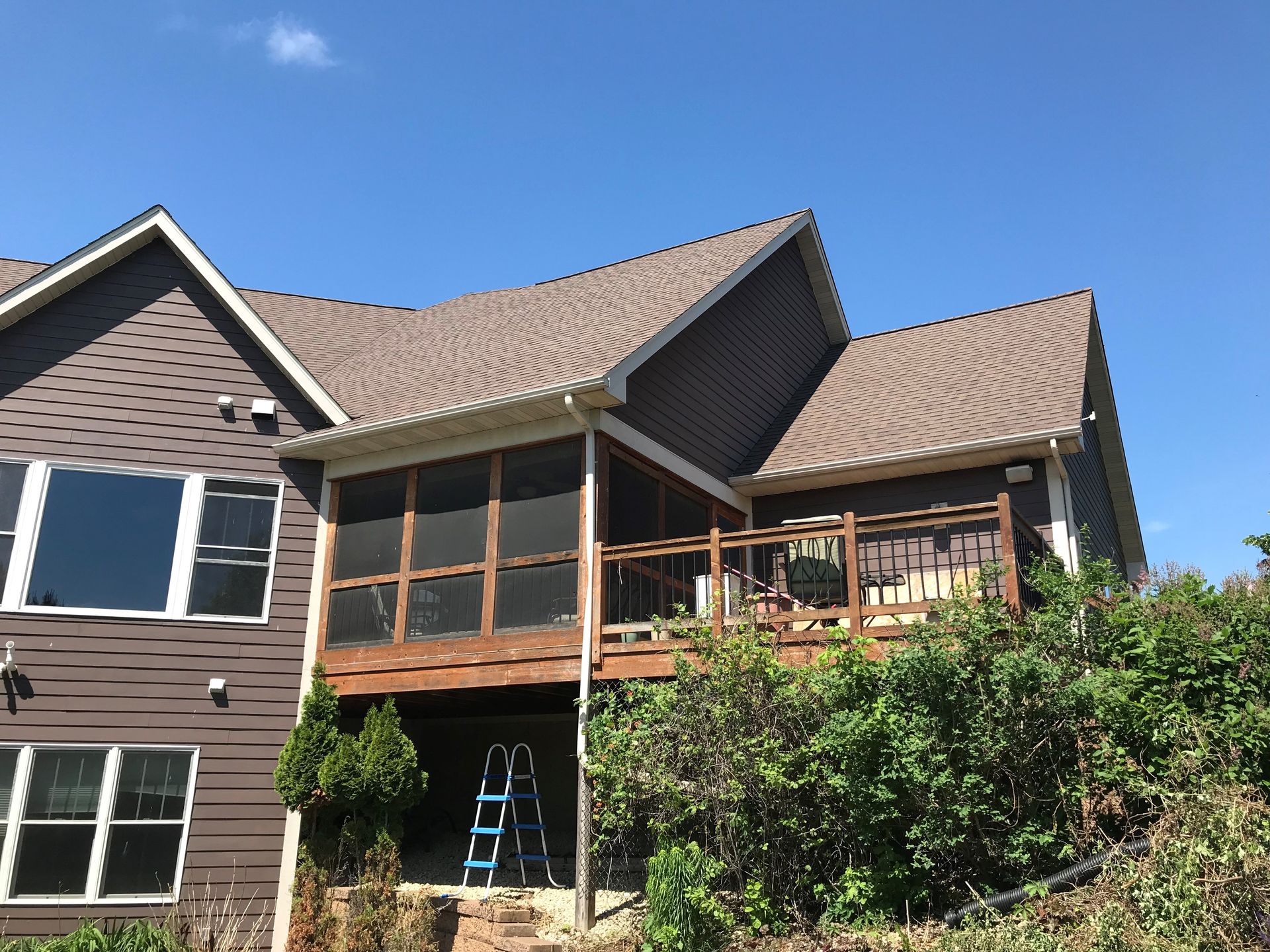 Brown house with screened porch and wooden deck, ladder, blue sky.
