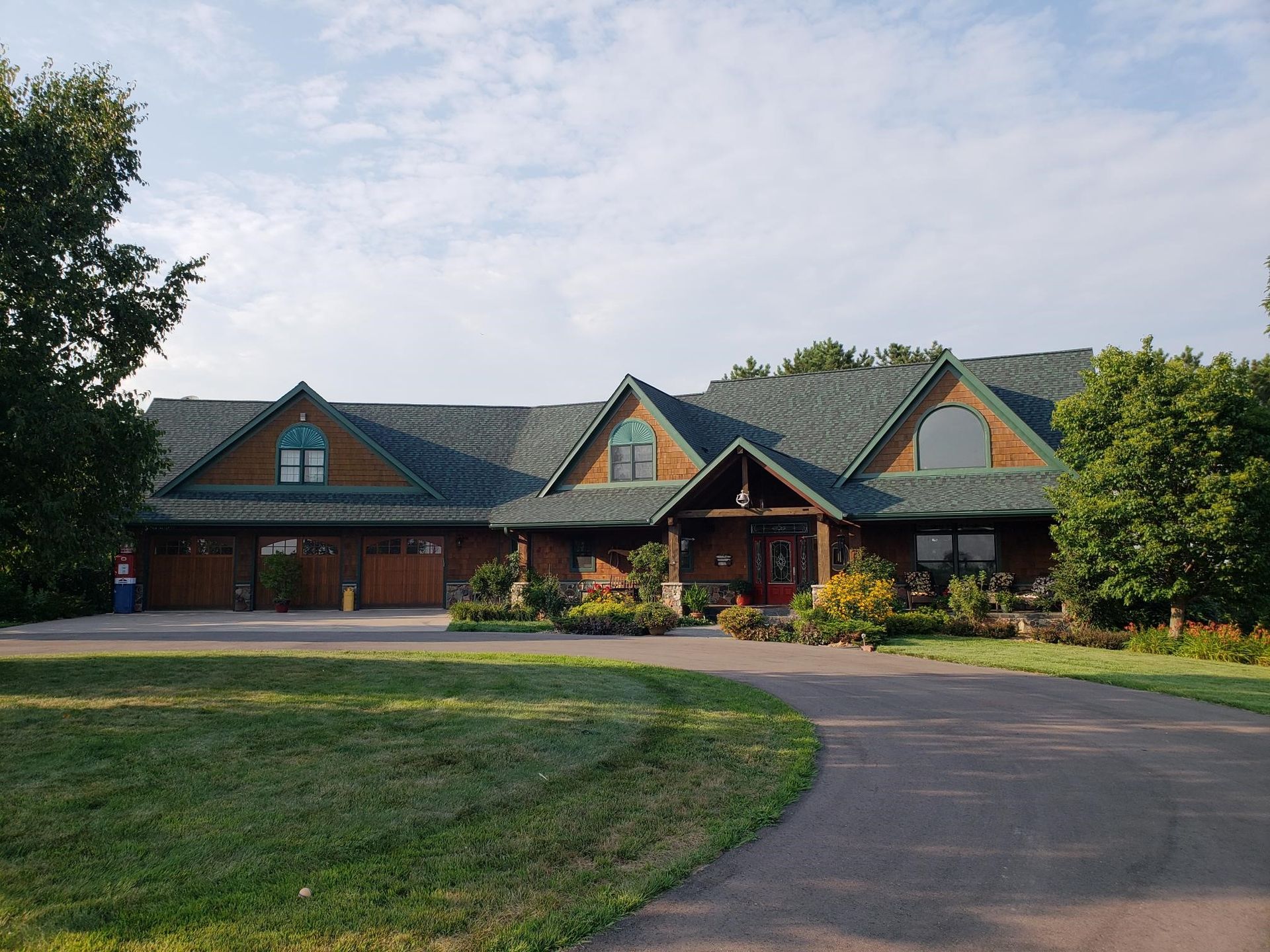 A large, brown house with a green roof and a circular driveway on a grassy lawn.