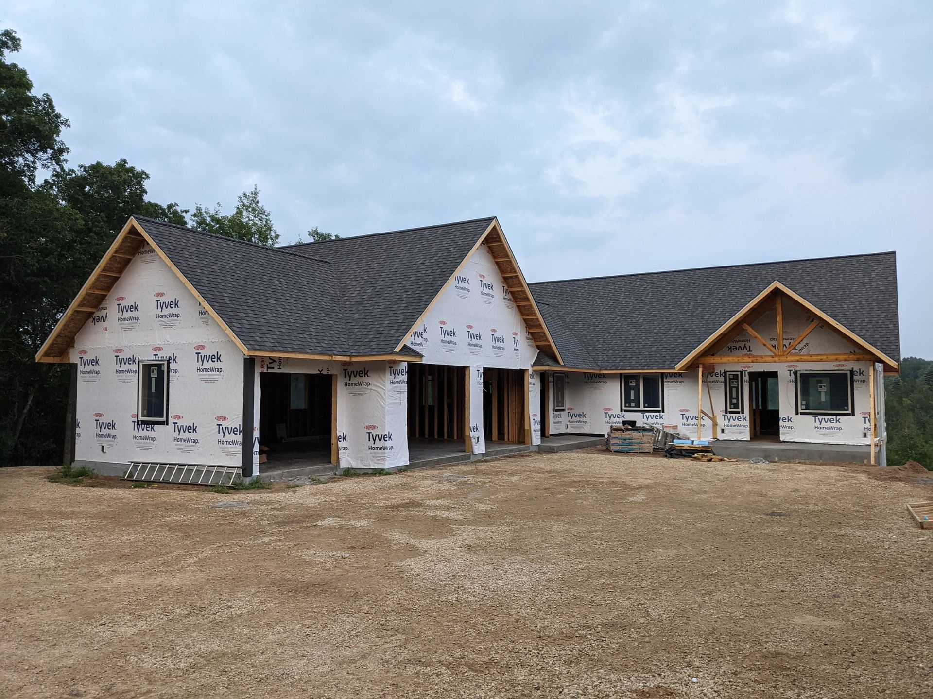 House under construction with a gray shingled roof and white exterior wrap.