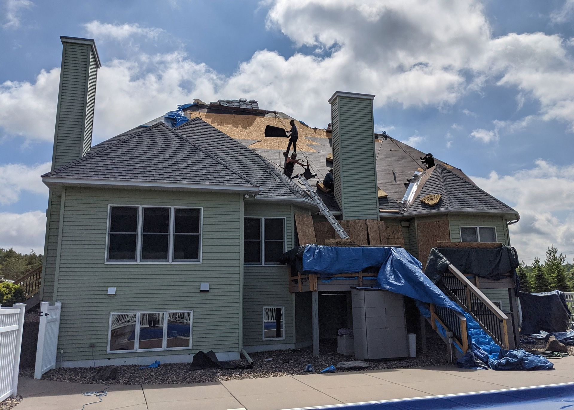 House with significant roof damage, covered by a blue tarp. The pool is visible in the foreground.