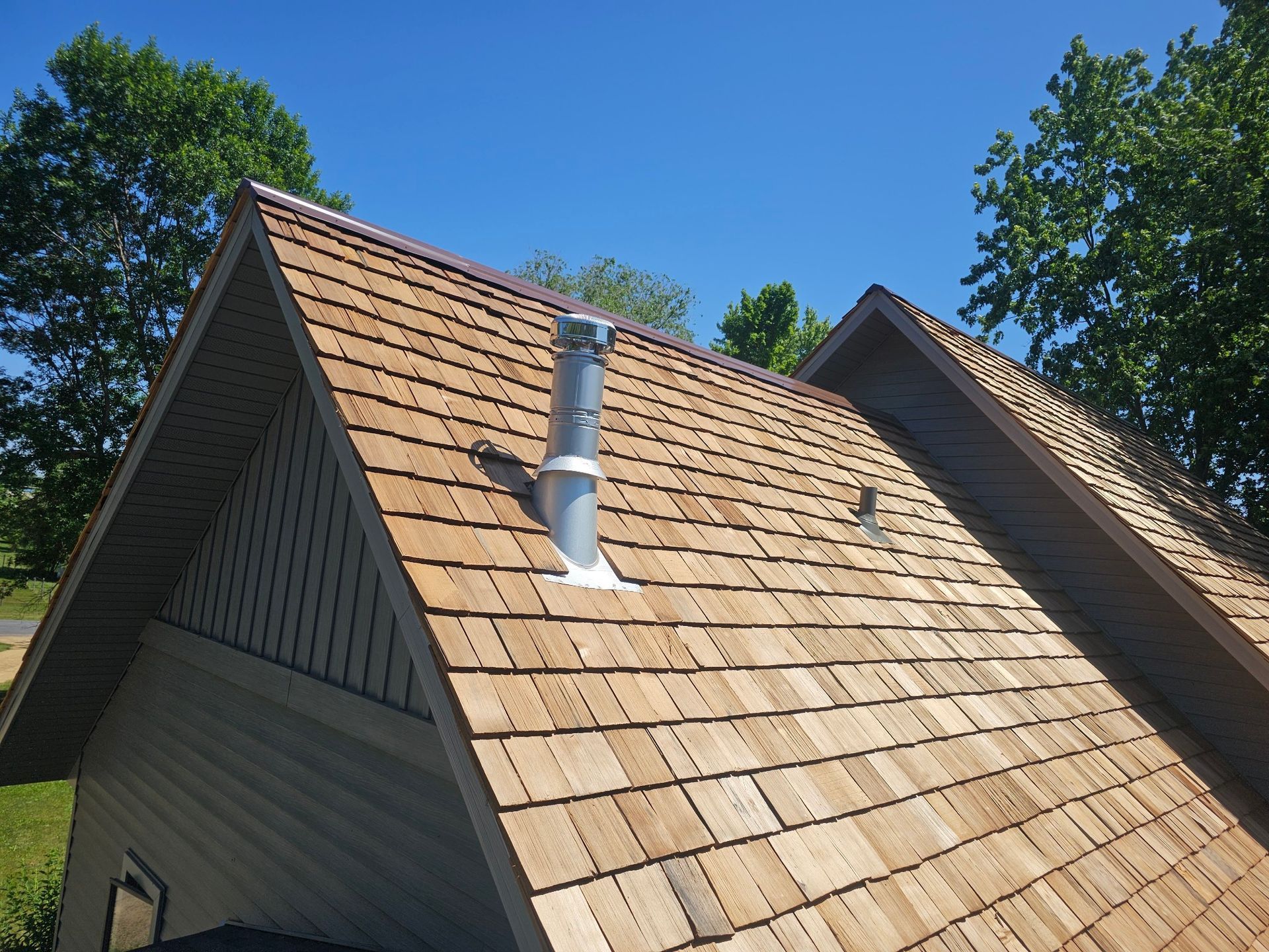 Wood shingle roof with a metal vent pipe and blue sky background.