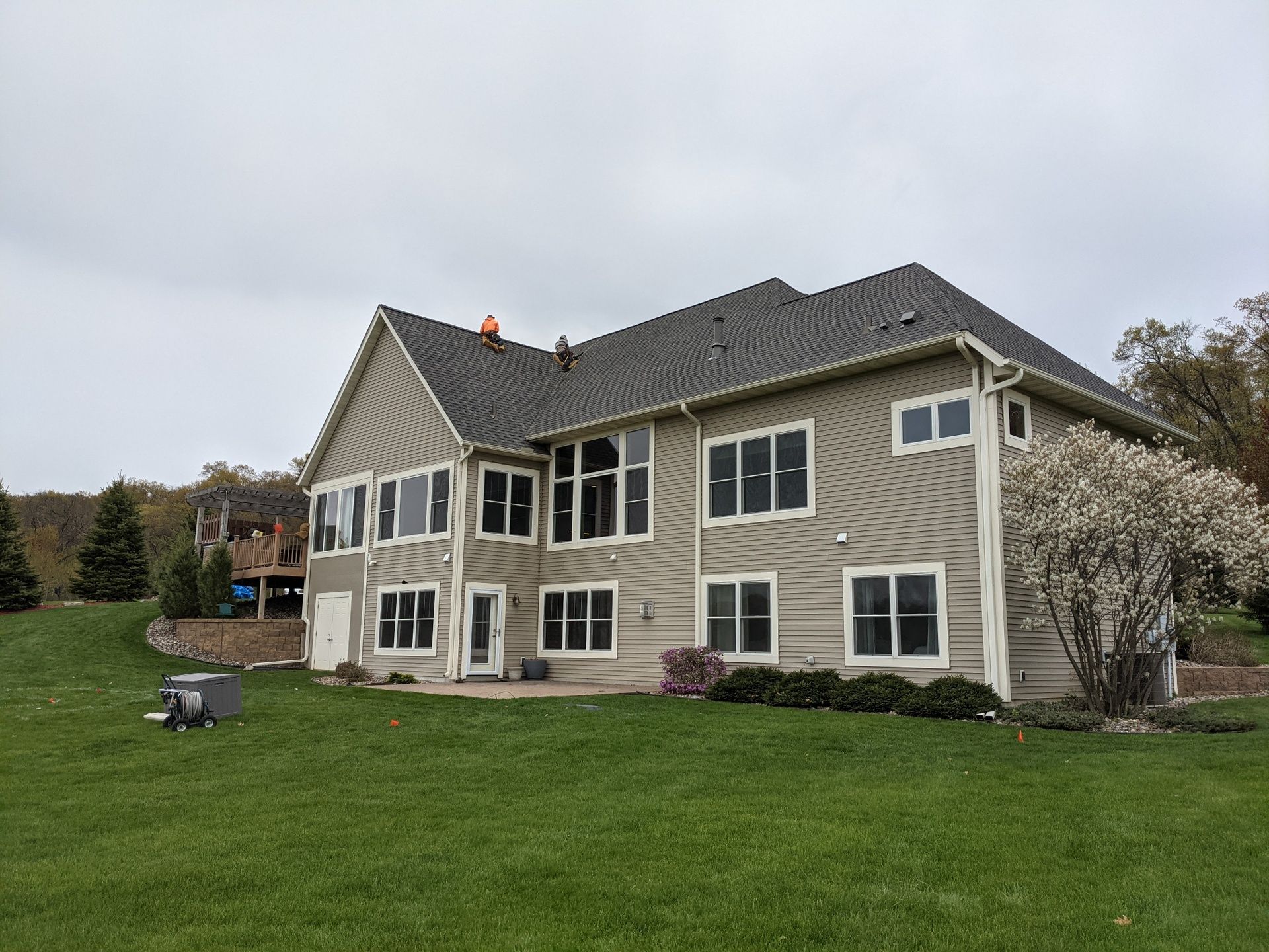 Large two-story house with gray siding, multiple windows, and a grassy lawn under a cloudy sky.