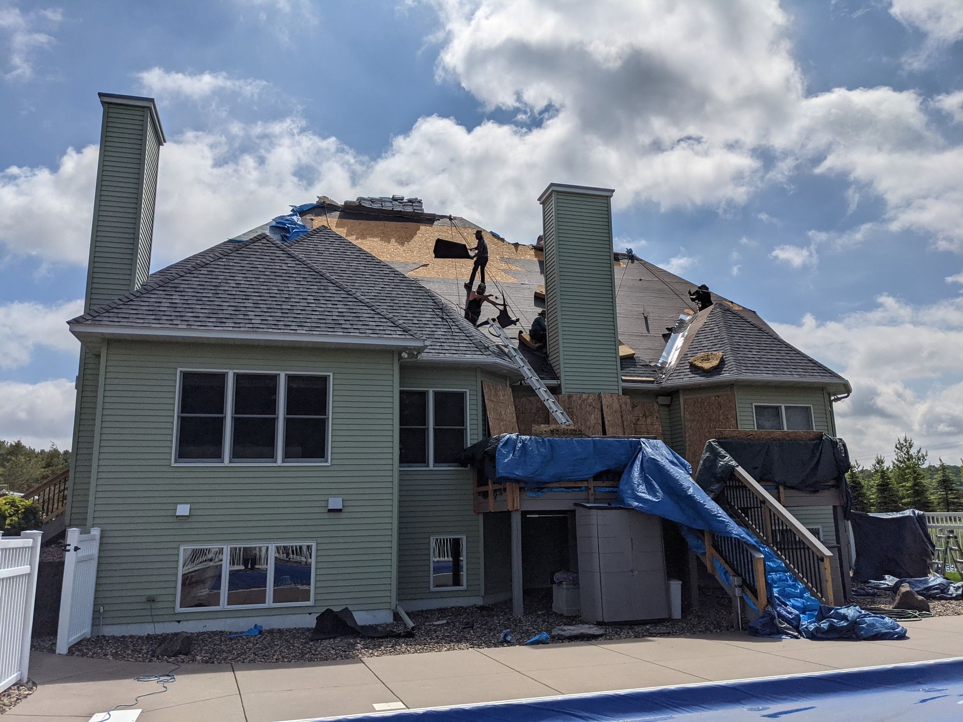 House with extensive roof damage, blue tarp covering part of the back deck, under a partly cloudy sky.