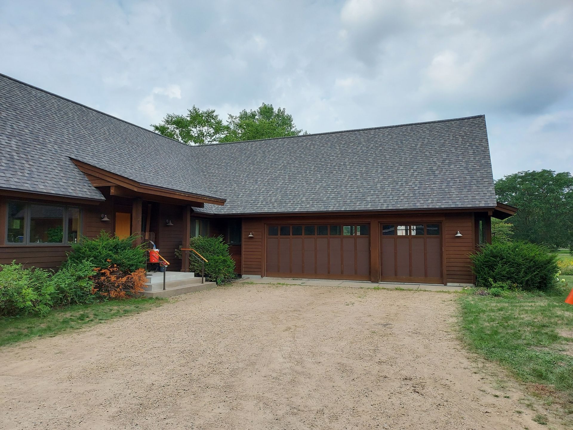Brown house with a gravel driveway and two-car garage; cloudy sky.