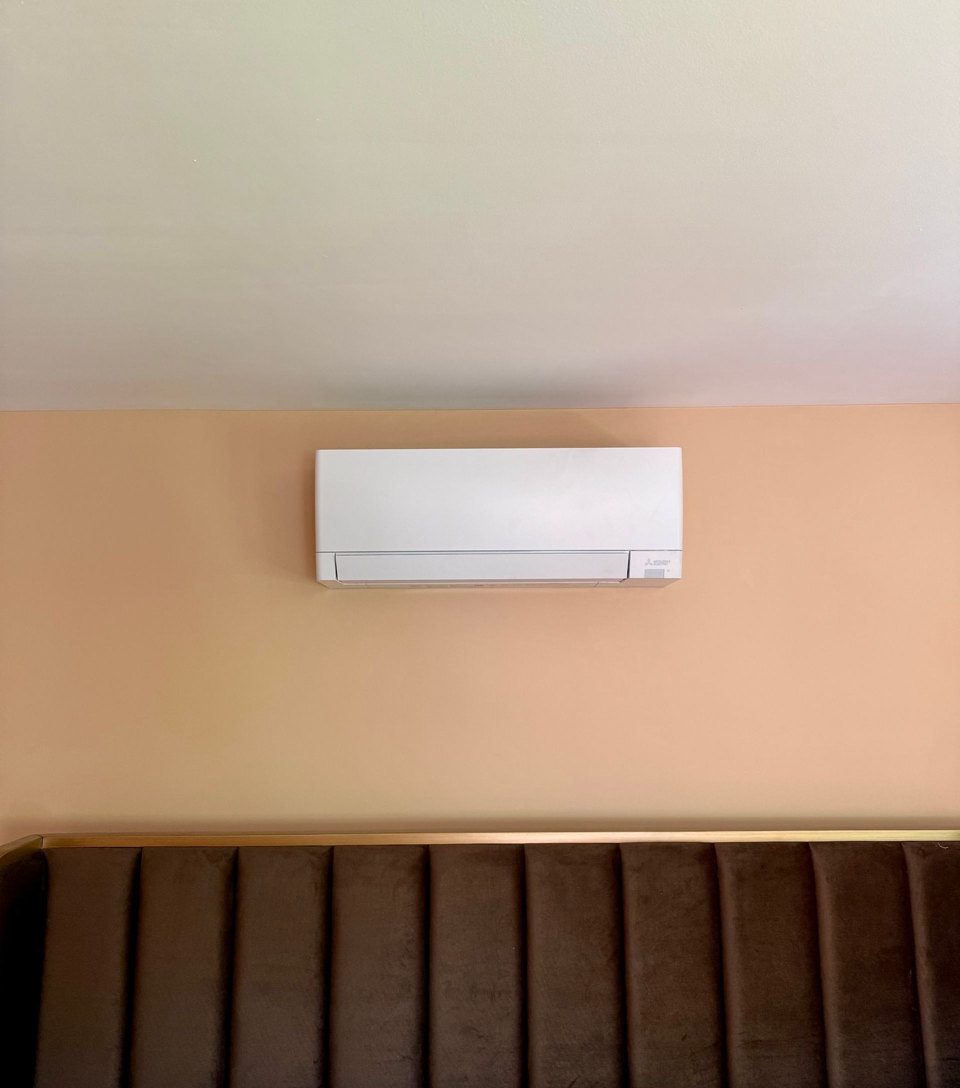 Wall-mounted white air conditioner near a window with sheer curtains in a beige room
