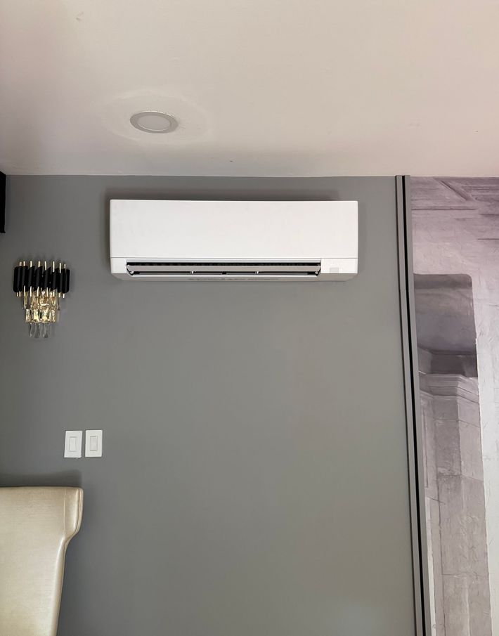 White wall-mounted air conditioner in a beige room near a bright window.