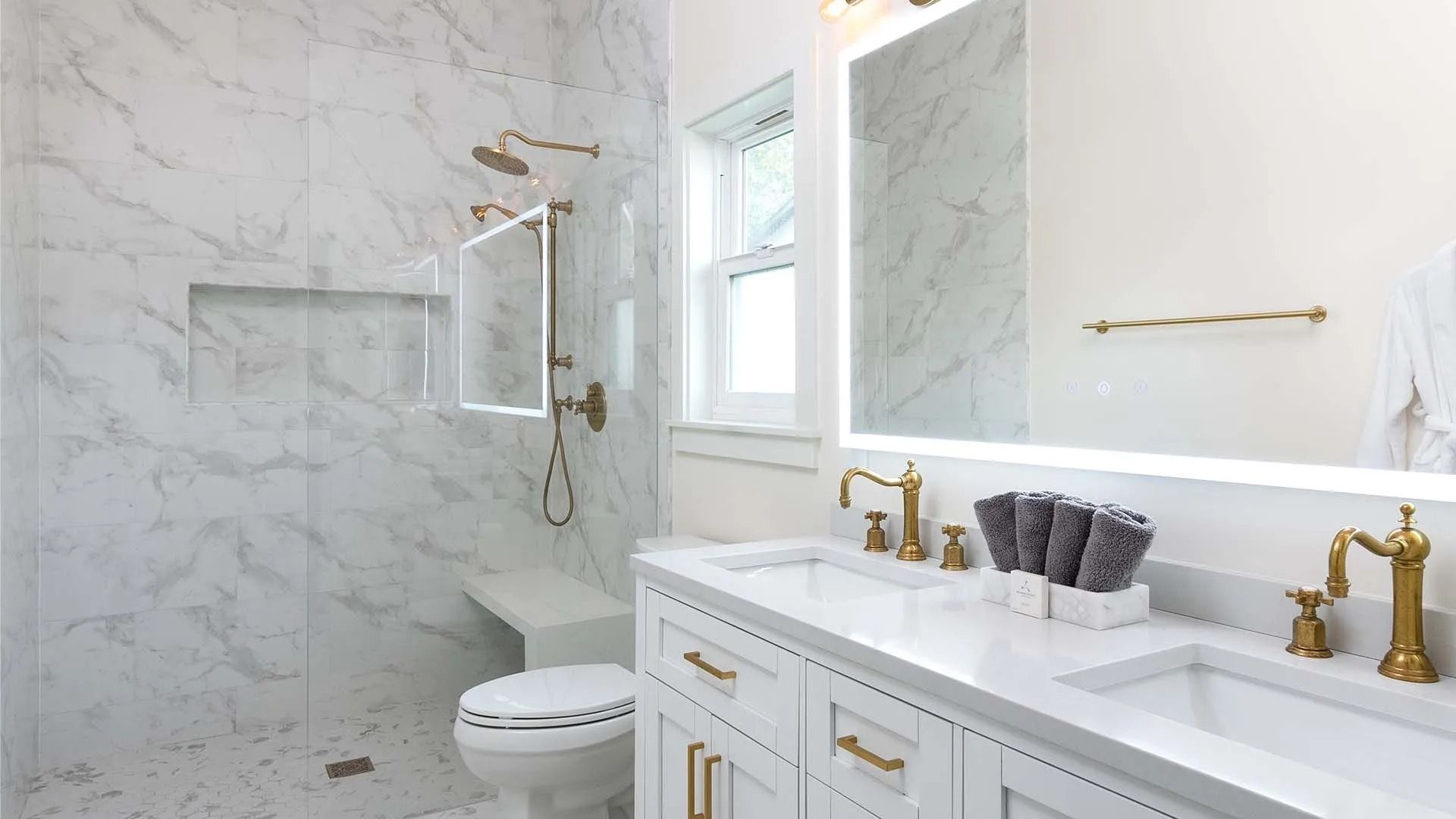 Bright marble bathroom with glass shower, white vanity, and gold fixtures