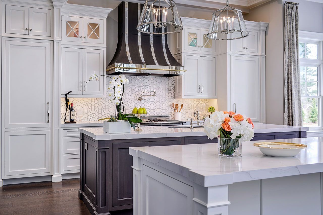 Bright white kitchen with dark island, marble counters, stainless hood, and fresh flowers on the island.