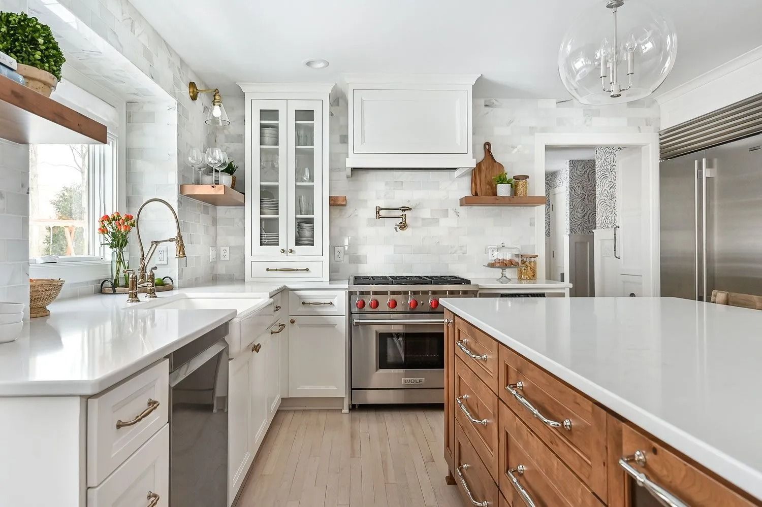 Bright modern kitchen with white cabinets, marble counters, stainless stove, and wood island drawers