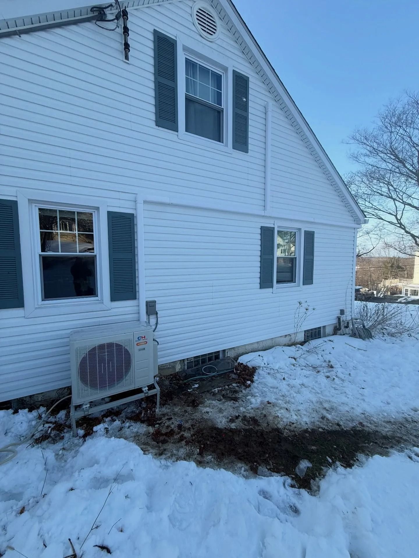 Snowy white house exterior with blue shutters and an air conditioning unit.