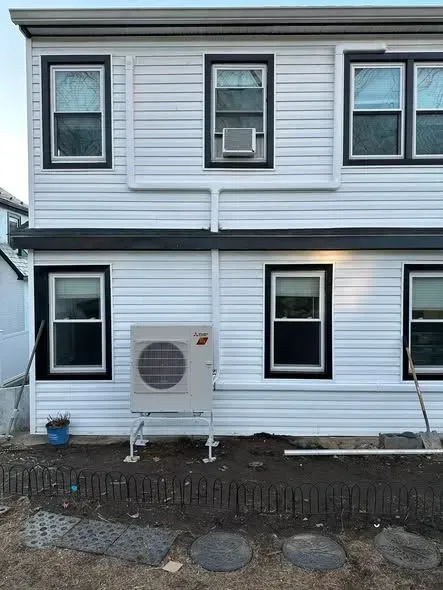 White two-story house exterior with windows, an air-conditioning unit, and small yard at ground level
