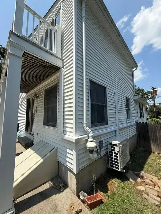 White-sided house exterior with balcony, windows, and an air conditioner unit by the foundation