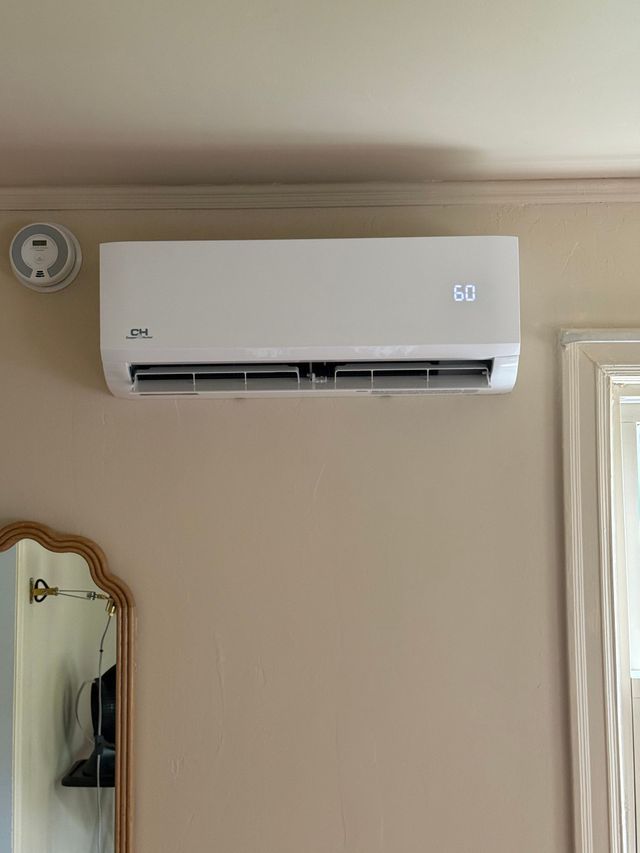 Wall-mounted white air conditioner above a mirror on a beige wall.
