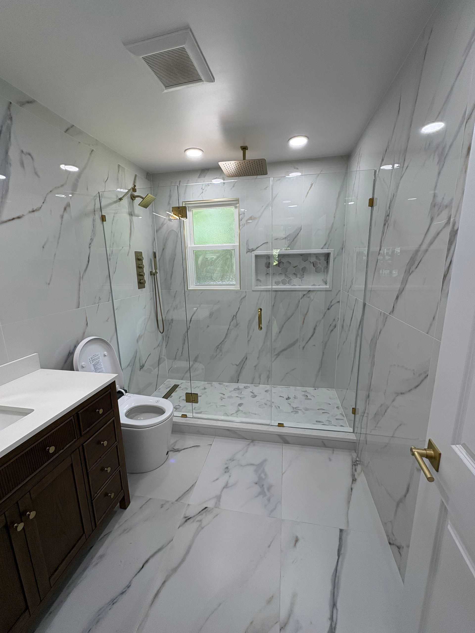 Bright marble-tiled bathroom with shower, toilet, sink, and window