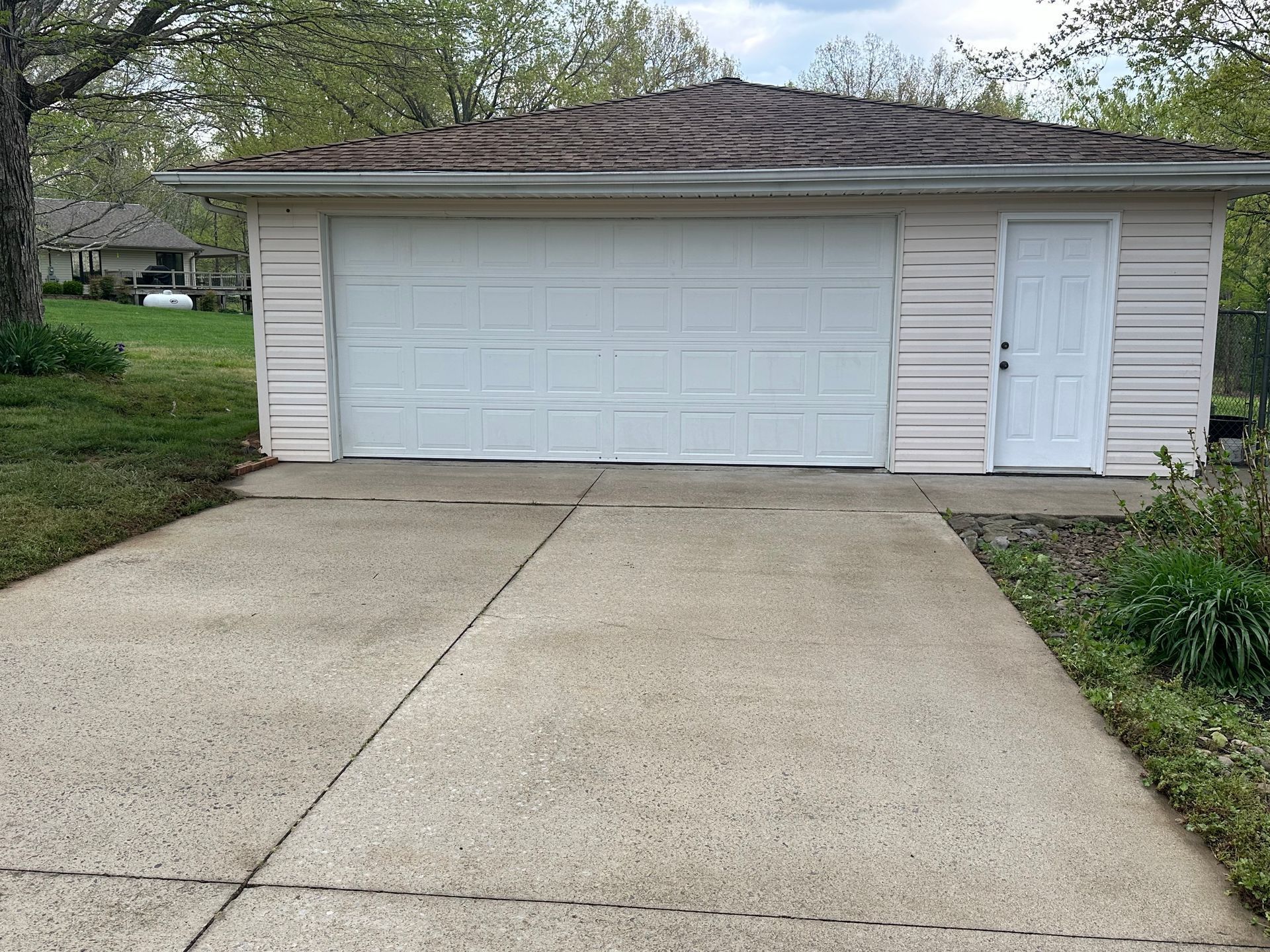 Garage with a white door, siding, and brown roof. Concrete driveway in front.