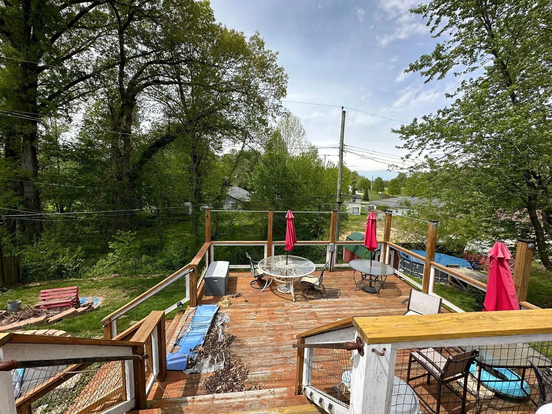 Wooden deck with tables, pink umbrellas, and surrounding trees under a cloudy sky.