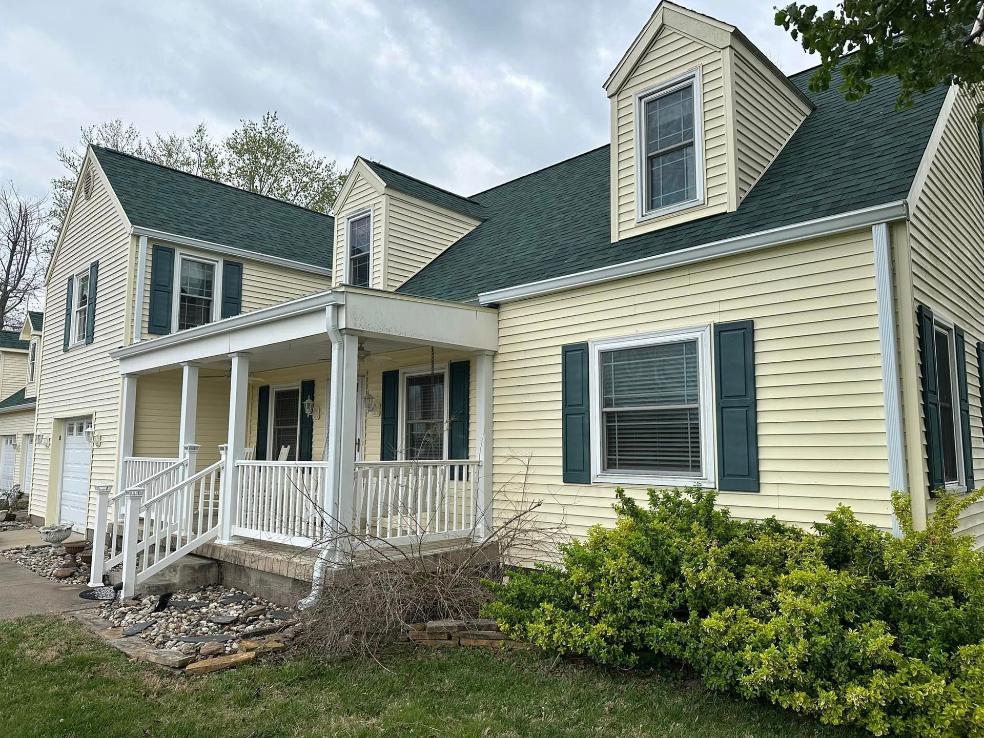 Yellow house with green roof, shutters, and a porch, set in a yard.