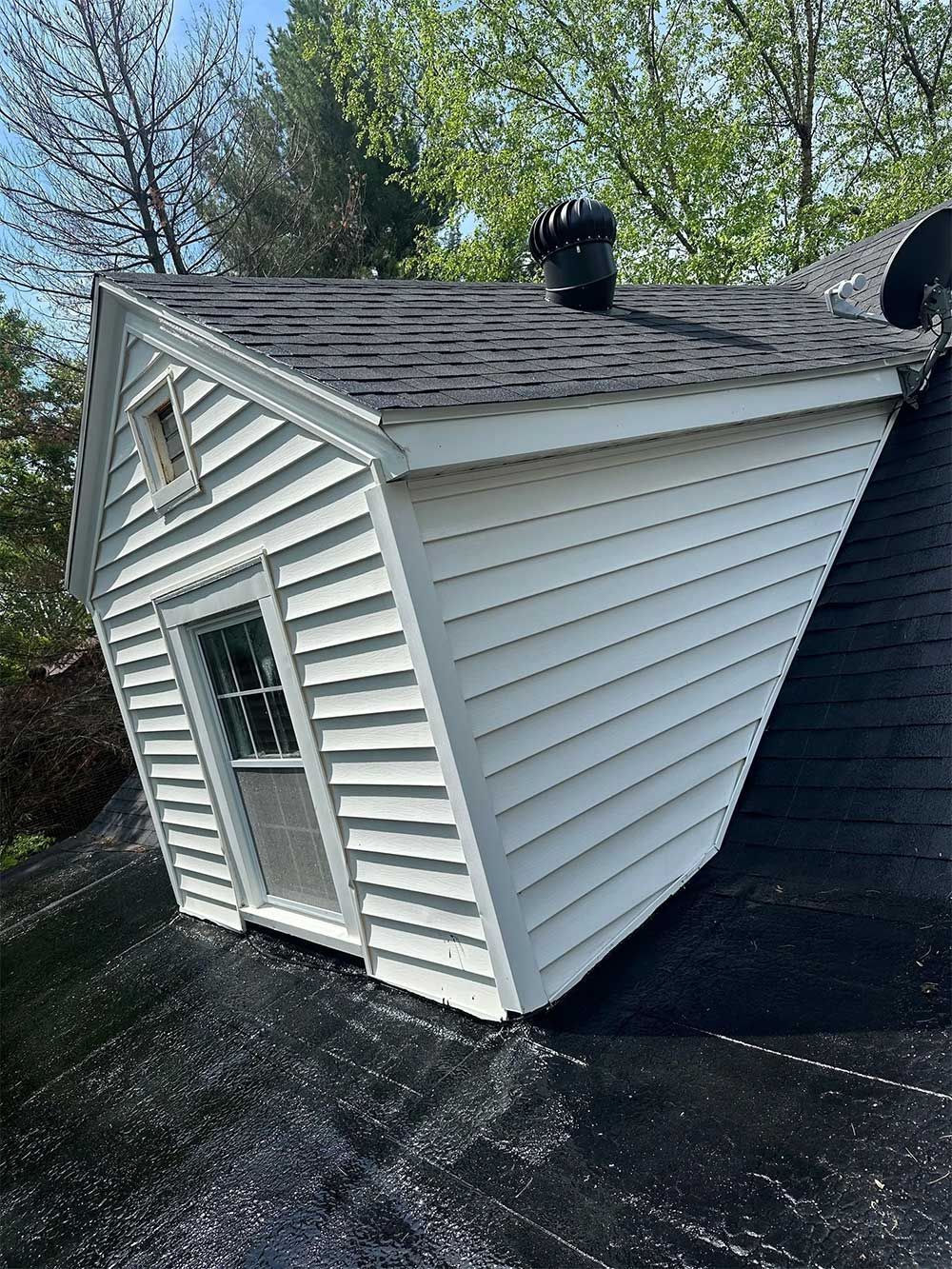 A small white building with a black roof and a chimney sits on a roof under a blue sky.